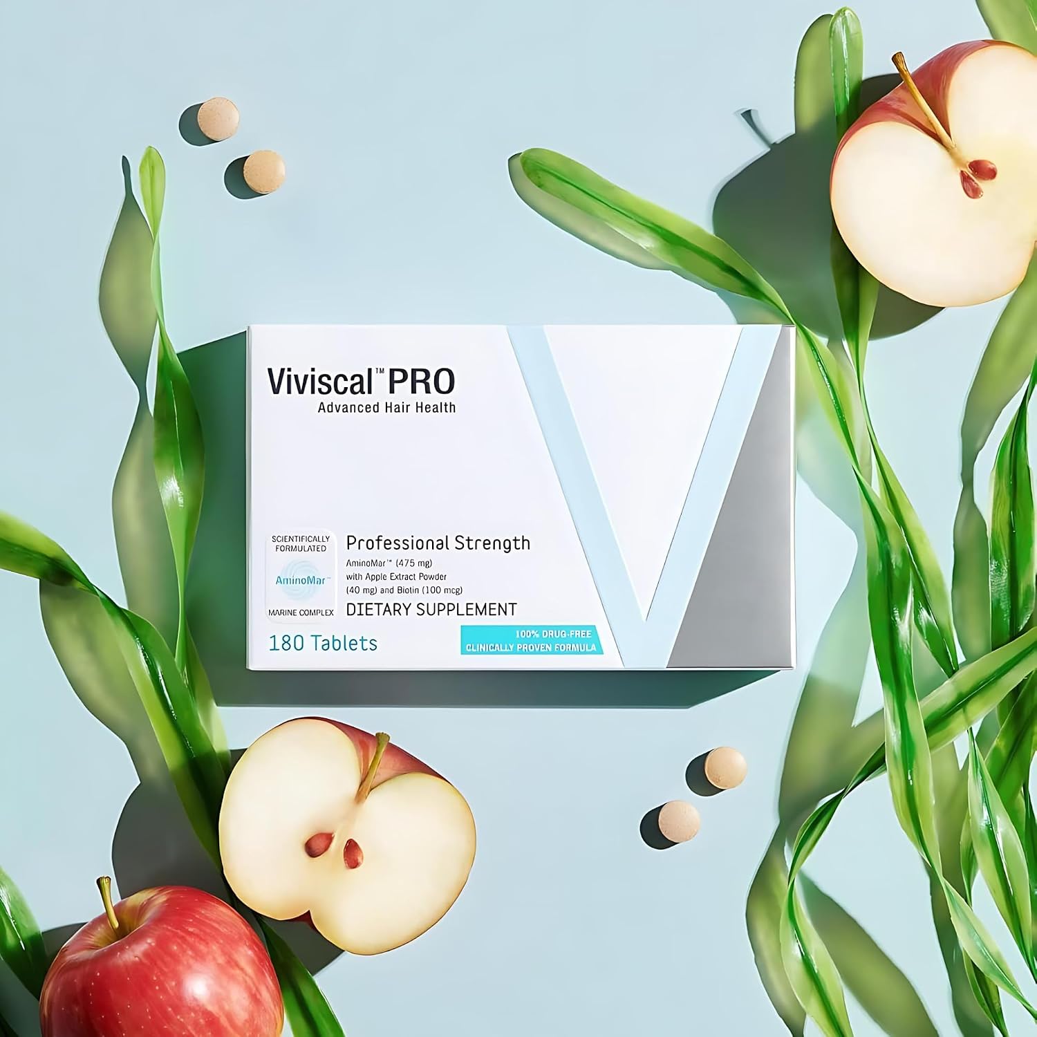 A box of Viviscal PRO Advanced Hair Health dietary supplement, styled in a flat-lay with fresh red apples and green leaves on a light blue background.