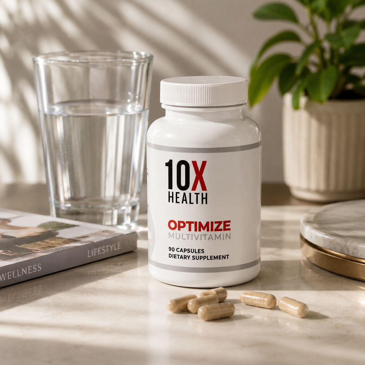 A white bottle of 10X Health Optimize Multivitamin dietary supplement with several beige capsules scattered in front, set on a marble surface next to a glass of water and a potted plant.